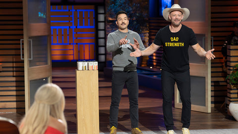 Dad Strength founders on Shark Tank stage, wearing 'Dad Strength' shirts.