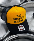 Yellow and black Dad Strength Brewing foam trucker hat with bold black logo, black mesh back, and curved black brim.