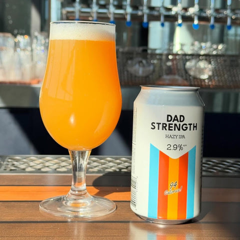 Glass of Dad Strength Hazy next to a can labeled 'Dad Strength Hazy IPA' on a bar counter.