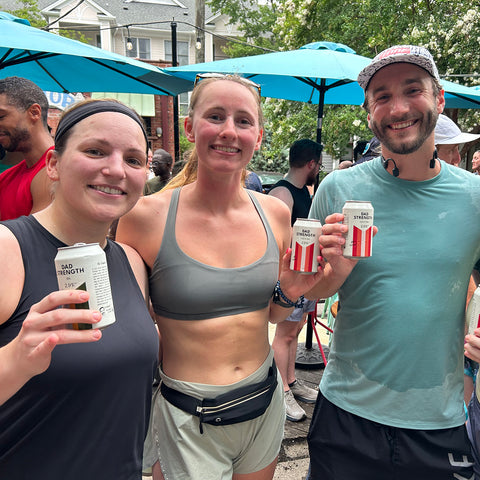 Three Dad Strength Brewing supporters holding cans of low-ABV craft beer at an outdoor community gathering.